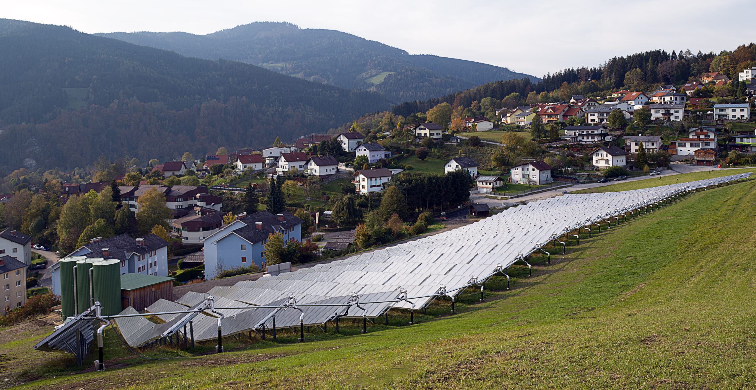 Solaranlage auf einem grünen Feld in Mürzzuschlag, dahinter sieht man die Häuser der Stadtgemeinde.