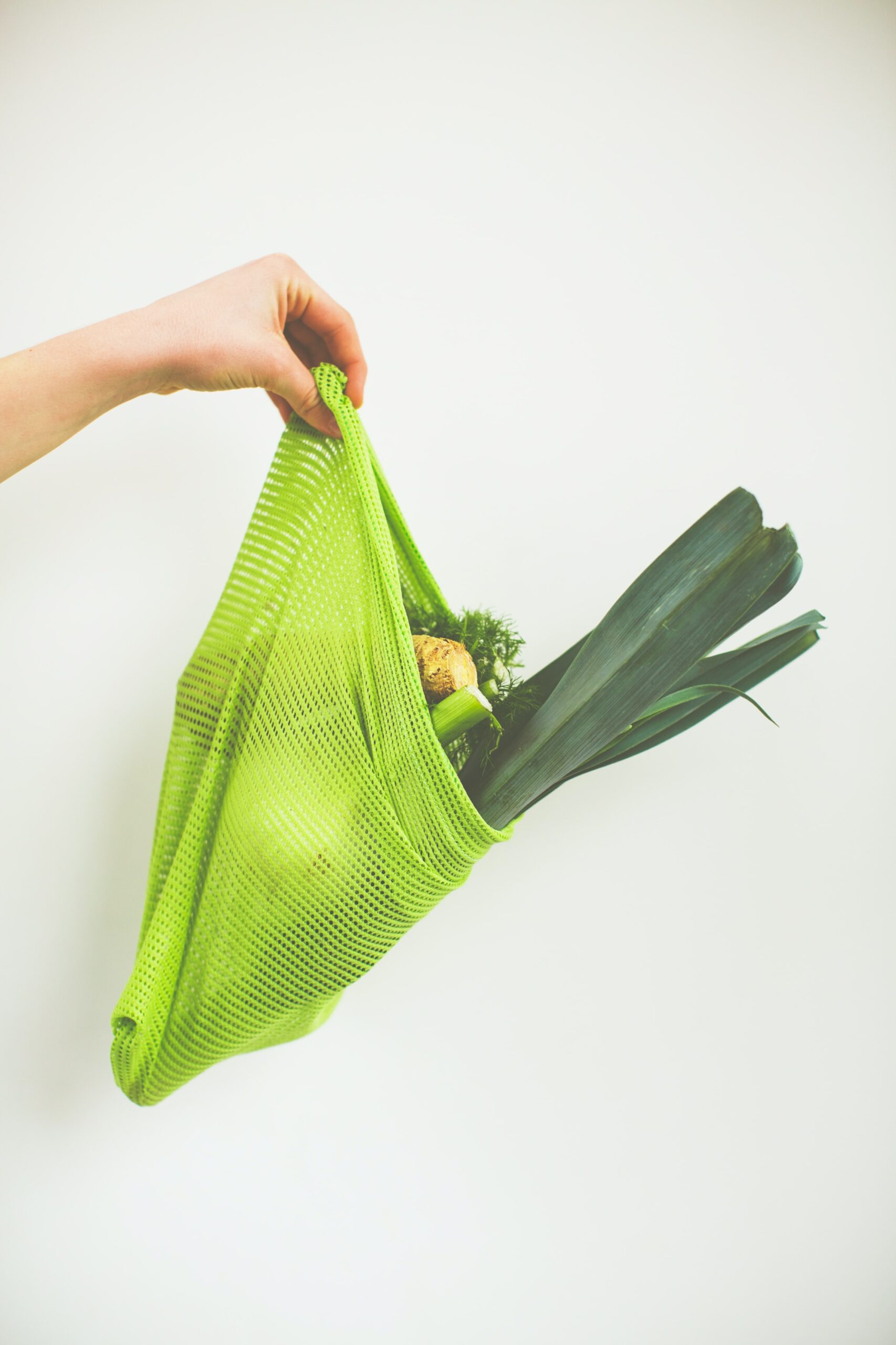 Eine Hand hält eine Plastikeinkaufstüte, die mit Gemüse gefüllt ist.
