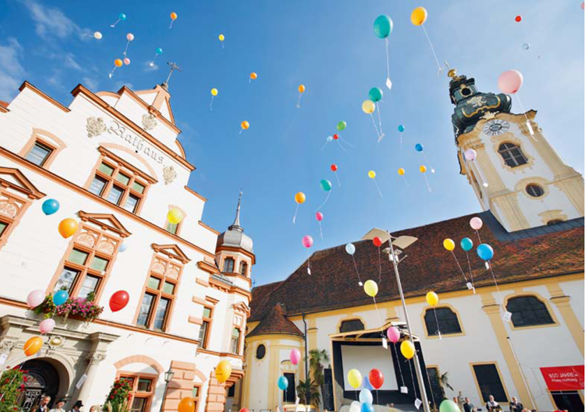 Am Hauptplatz Hartberg steigen viele bunte Luftballons in die Luft.