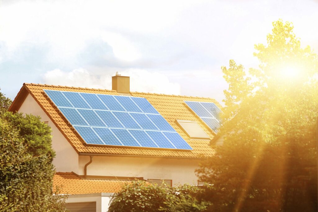 Solarpanele auf einem mit Ziegel gedeckten Dach, die Sonne scheint durch einen Baum, der vor dem Haus steht