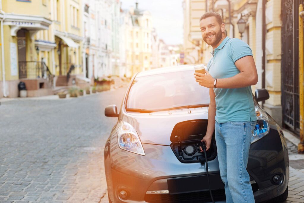 Ein Mann im kurzen T-Shirt steht vor einem Elektro-Auto und lädt es gerade